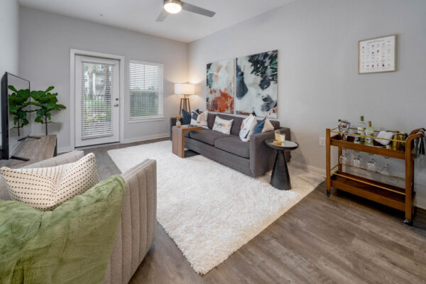 The Avery apartment living room with wood style floor, plush seating, large artwork, and balcony door.