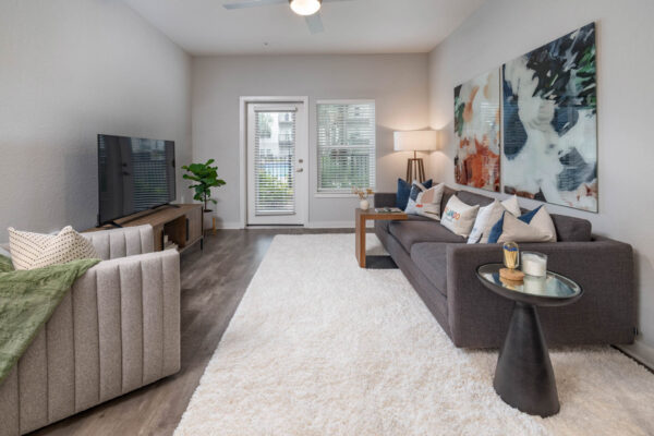 The Avery apartment living room with wood style floor, plush seating, large artwork, and balcony door.