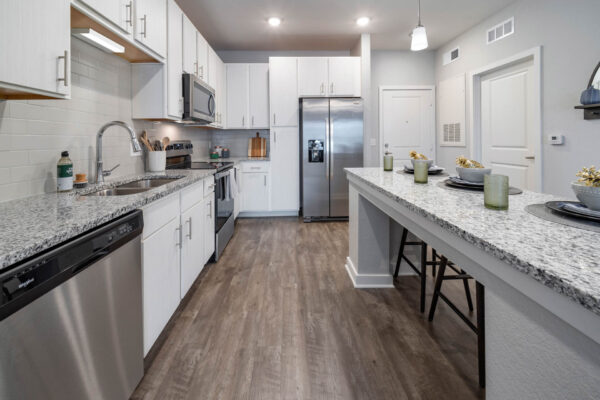 The Avery apartment kitchen with wood style floor, white cabinets, stone counters, and stainless steel appliances.