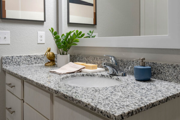 The Avery apartment bathroom with white cabinets, stone counters, and large mirror.
