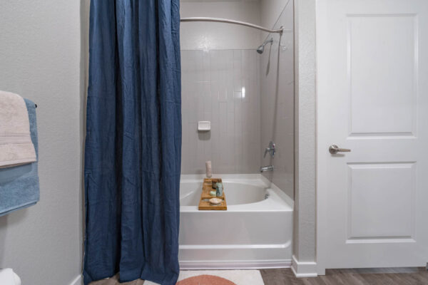 The Avery apartment bathroom with tiled shower tub and bath supplies.