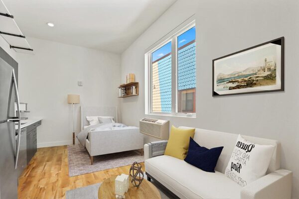 The Economist apartment living area with modern kitchen, couch, bed, and large windows.