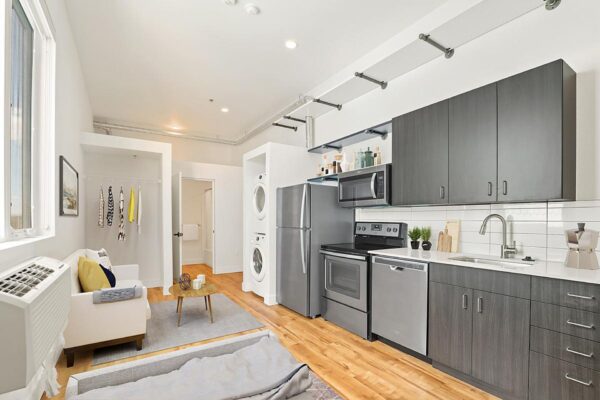The Economist apartment living area with modern kitchen, plush couch, and laundry closet.