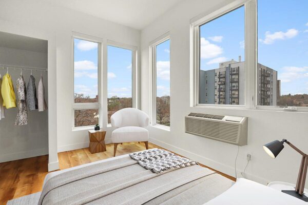 The Economist apartment living area with plush bed, large closet, and large windows.