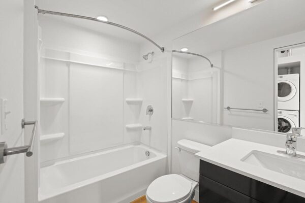 The Economist apartment bathroom with dark cabinets, light counters, large mirror, and shower tub.