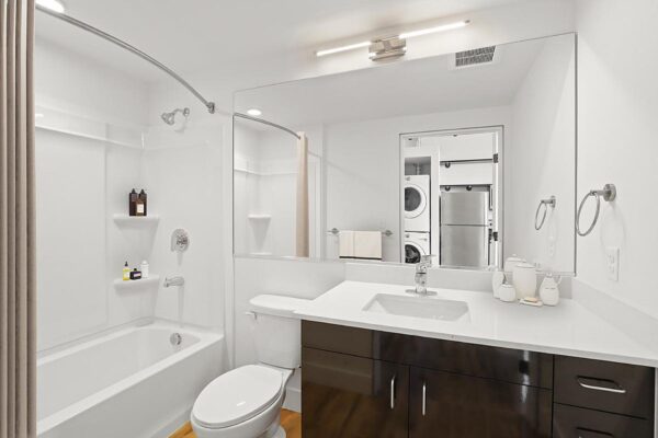 The Economist apartment bathroom with dark cabinets, light counters, large mirror, and shower tub.