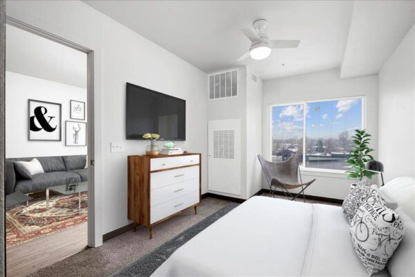 The Overland apartment bedroom with plush bed, dresser, TV, and large window.