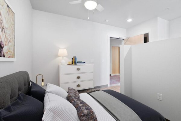 The Overland apartment bedroom with dresser, plush bed with headboard, and ceiling fan.