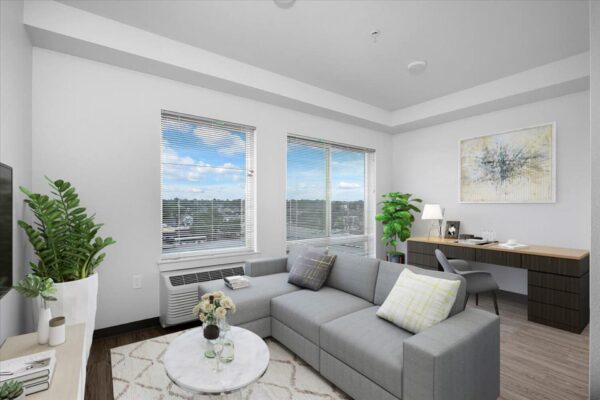 The Overland apartment living area with plush seating, desk, potted plants, and large windows.