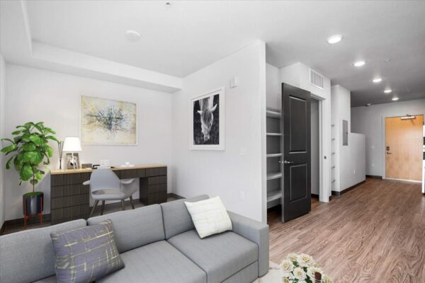 The Overland apartment living area with plush couch, desk, wall art, and closet.