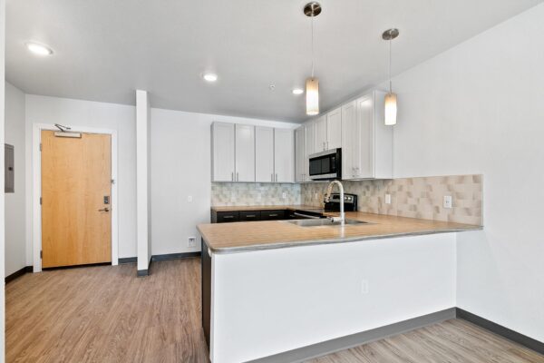 The Overland apartment kitchen with wood style floor, two tone cabinets, and tiled backsplash.