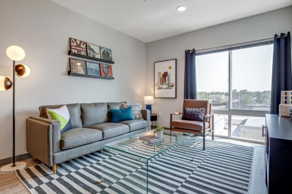 The Overland apartment living room with pattern rug, plush seating, wall art, and large window.