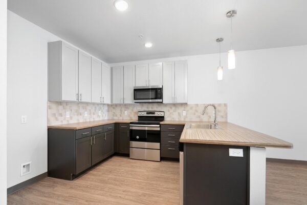 The Overland apartment kitchen with wood style floor, two tone cabinets, and stainless steel range.