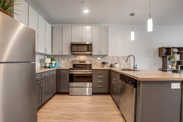 The Overland apartment kitchen with wood style floor, two tone cabinets, and stainless steel appliances.