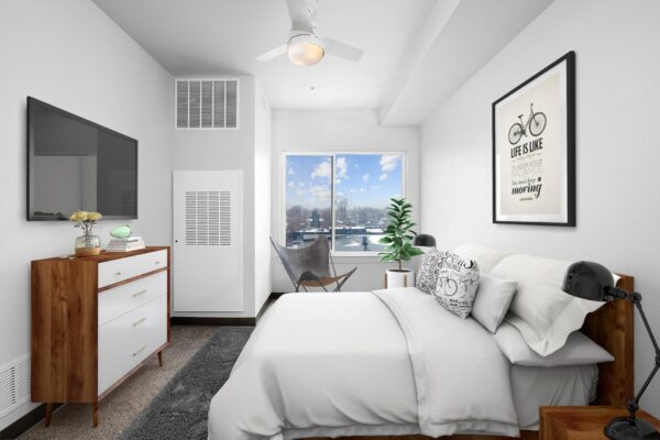 The Overland apartment bedroom with plush bed, dresser, TV, and large windows.