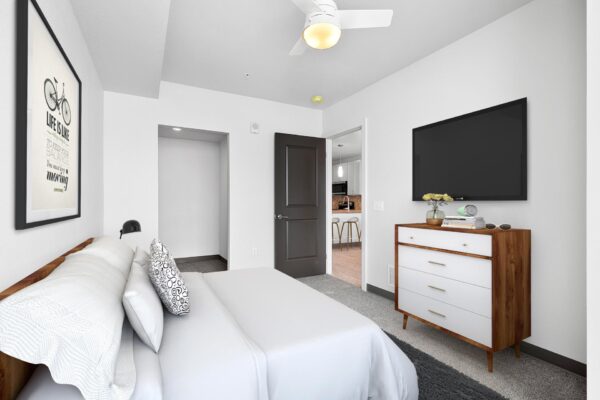 The Overland apartment bedroom with plush bed, dresser, TV, and large windows.