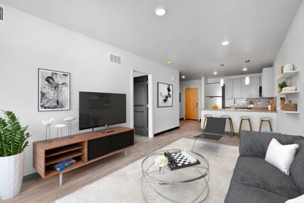 The Overland apartment living room with plush seating, console with TV, wall art, and modern kitchen.