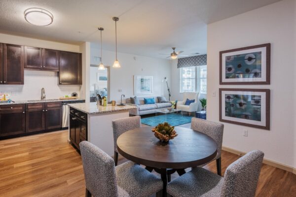 The Point at Bella Grove apartments dining area, wood style floor, dark wood cabinets, quartz counters, lighting fixtures, kitchen island, lighting fixtures, stainless steel appliances and showcasing living room area.