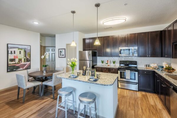 The Point at Bella Grove apartments kitchen with dining area, wood style floor, dark wood cabinets, quartz counters, lighting fixtures and stainless steel appliances.