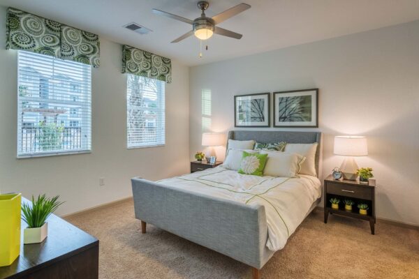 The Point at Bella Grove apartments bedroom with plush bed, plush carpet, large windows, bedside tables with lamps, and ceiling fan.