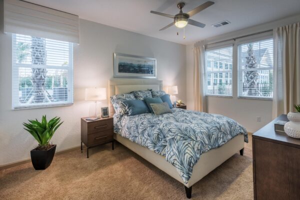The Point at Bella Grove apartments bedroom with plush bed, plush carpet, large windows, bedside tables with lamps, and ceiling fan.