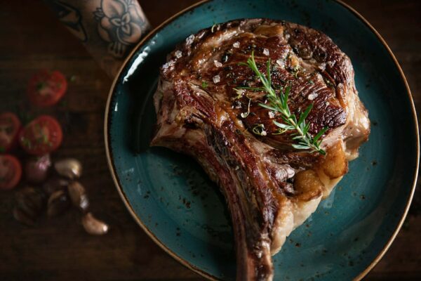 Grilled steak with rosemary on a rustic blue plate.