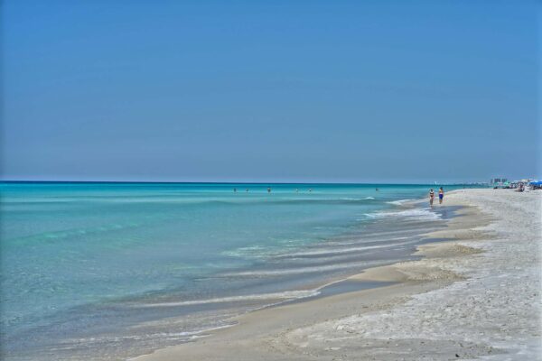 Sandy Florida beach with beachgoers walking in the water.