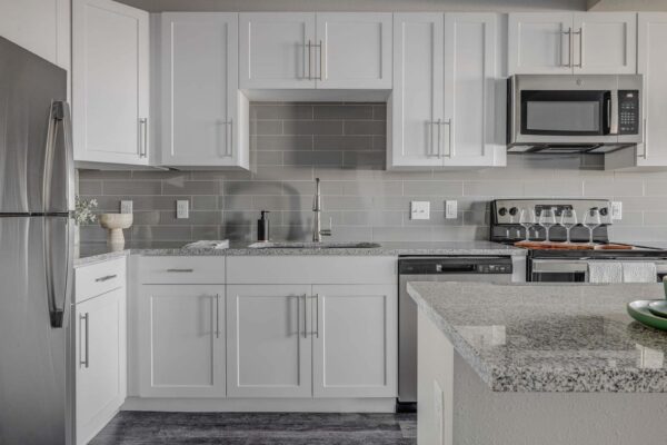 Copper 87 apartments with wood style floor, white cabinets, stone counters, and stainless steel appliances.