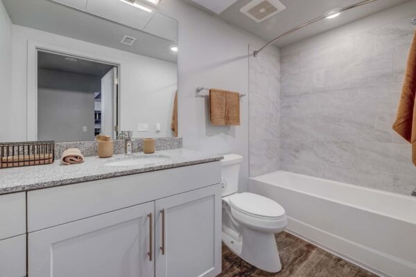 Copper 87 apartments bathroom with wood cabinets, stone counters, and large mirror.