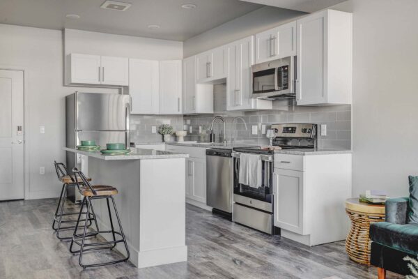 Copper 87 apartments kitchen with wood style floor, white cabinets, stone counters, and stainless steel appliances.