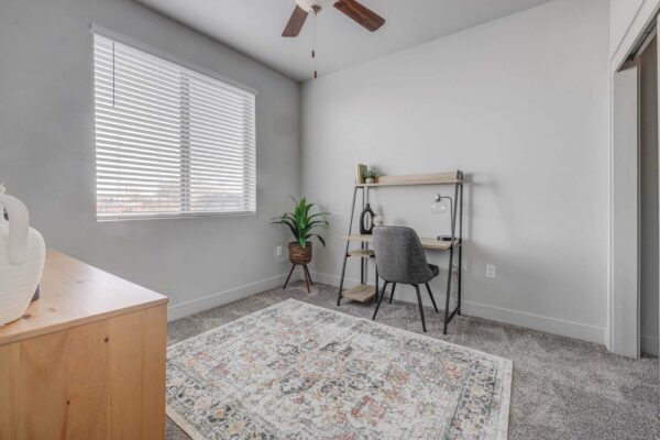 Copper 87 apartments den with plush carpet, desk, and large windows.