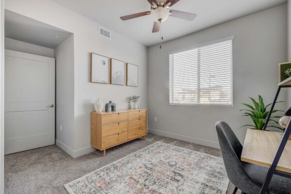 Copper 87 apartments den with plush carpet, dresser, framed art, and large window.