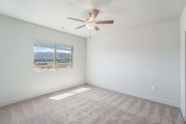 The Marc at Monument Ridge apartment bedroom with plush carpet, ceiling fan, and large window.