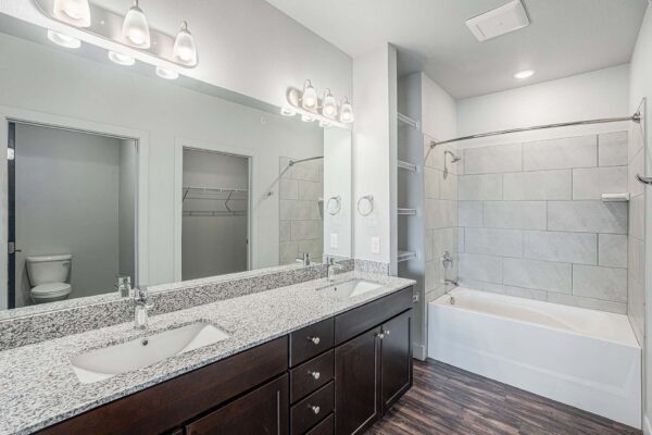 The Marc at Monument Ridge apartment bathroom with wood cabinets, stone counters, and large mirror.