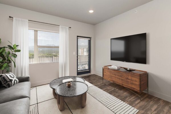 The Marc at Monument Ridge apartment living room with plush couch, wall mounted TV, and balcony door.