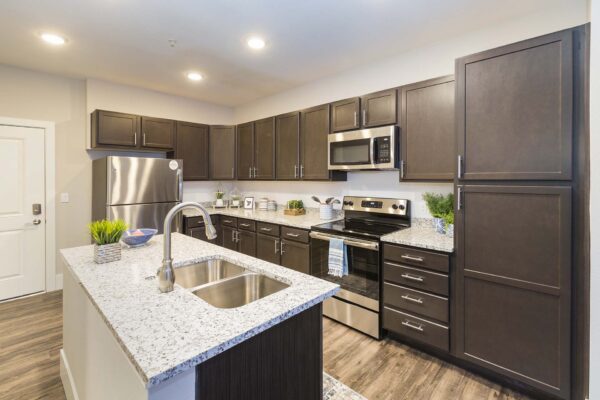 Retreat at Patriot Park apartment kitchen with wood style floor, wood cabinets, granite counters, and stainless steel appliances.