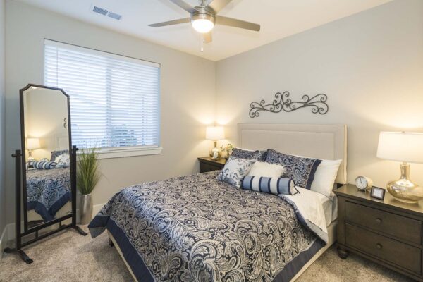 The Retreat at Patriot Park apartment bedroom with plush bed, bedside tables with lamps, and large window.