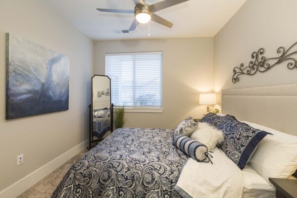 The Retreat at Patriot Park apartment bedroom with plush bed, bedside tables with lamps, and large window.