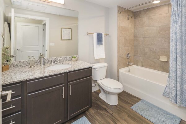 The Retreat at Patriot Park apartment bathroom with granite counters, tiled shower tub, and large mirror.