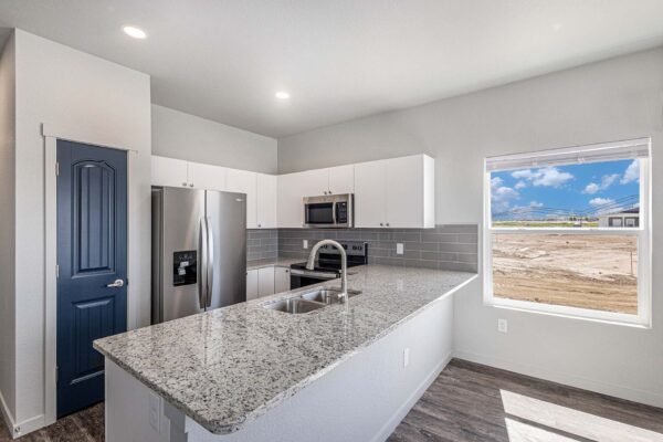 The Cottages at Woodmen Heights apartment kitchen with wood style floor, white cabinets, stone counters, and stainless steel appliances.