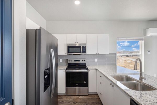 The Cottages at Woodmen Heights apartment kitchen with wood style floor, white cabinets, stone counters, and stainless steel appliances.