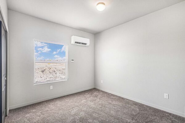 The Cottages at Woodmen Heights apartment bedroom with plush carpet and large window.
