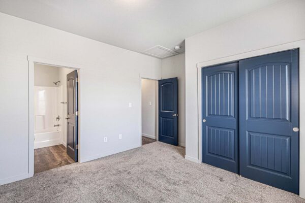 The Cottages at Woodmen Heights apartment bedroom with plush carpet and large blue closet doors.