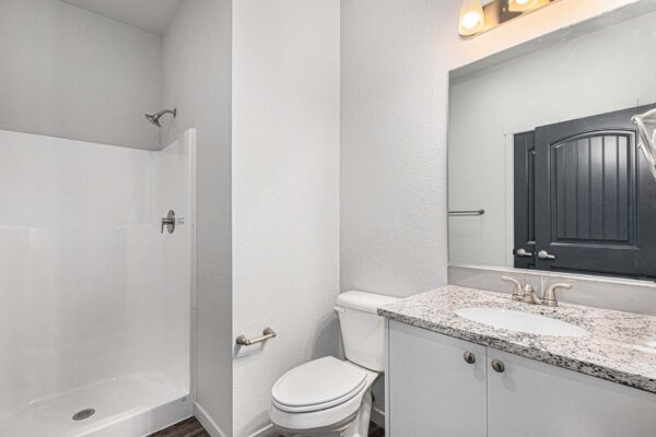 The Cottages at Woodmen Heights apartment bathroom with wood style floor, white cabinets, stone counters, and shower.