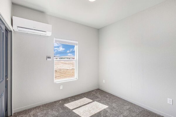 The Cottages at Woodmen Heights apartment bedroom with plush carpet and large window.