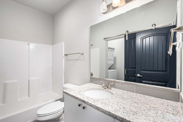 The Cottages at Woodmen Heights apartment bathroom with white cabinets, stone counters, and shower tub.