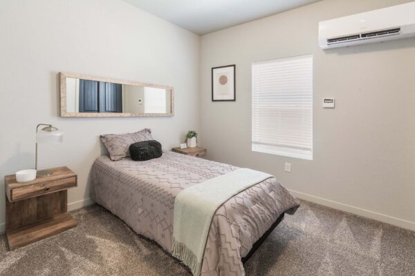 Cottages at Woodmen Heights apartment bedroom with carpet, plush bed, and bedside tables with decor.