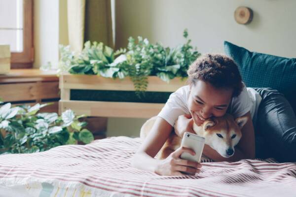 Person taking a selfie on a bed next to their Shiba Inu dog.